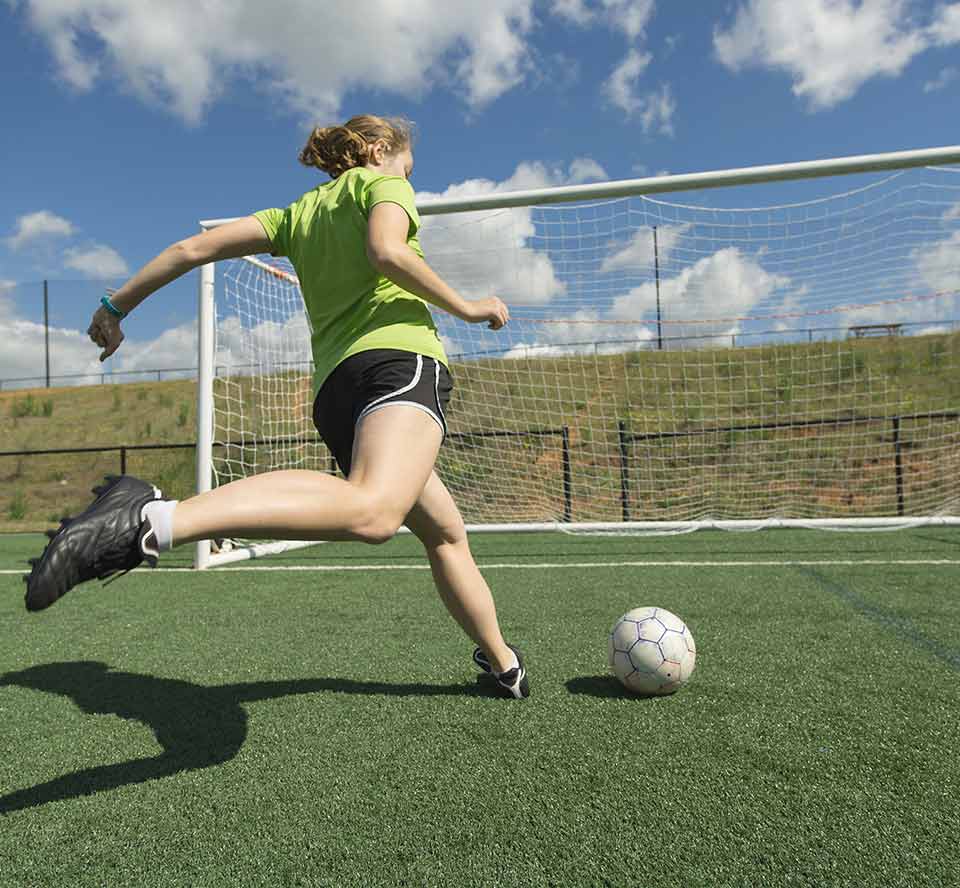 teenage girl about to kick a soccer ball into a goal